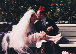 Newly married Glenda and Darrell sitting on a park bench, kissing